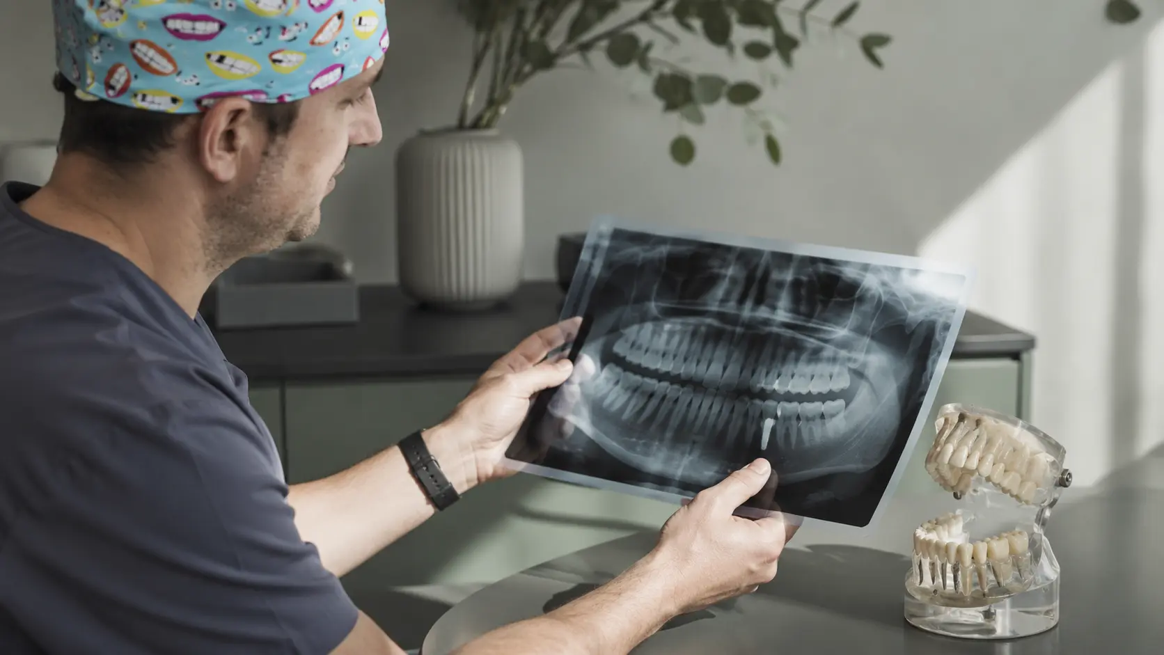 primer plano de manos de un profesional dental sosteniendo con cuidado una radiografía panorámica o un modelo anatómico de maxilar sobre una mesa de consulta, en un ambiente clínico moderno y minimalista